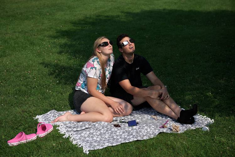 Grace Pease, of Tunbridge, and Dominick Small, of South Royalton look skyward from the green in South Royalton, Vt., as the moon obscures just over 60 percent of the sun in a solar eclipse Monday afternoon, August 21, 2017. (Valley News - James M. Patterson) Copyright Valley News. May not be reprinted or used online without permission. Send requests to permission@vnews.com.